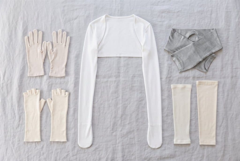 Bamboo gloves, fingerless gloves, a stay-on scratch-mitt cardigan, children's mitten sleeves and two arm sleeves laid flat on a bedsheet
